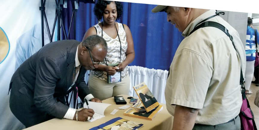 Co-author signing his book 'Reflections' for a reader at a live convention booth